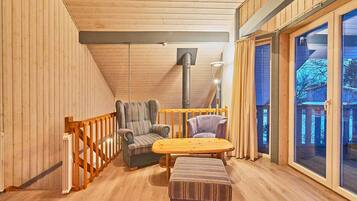 Una habitación acogedora con paredes de madera y techo inclinado, que incluye una mesa de madera y dos sillas acolchadas, un banco, y un gran ventanal con vistas.