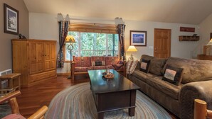 A cozy living room with a wooden coffee table, a brown leather sofa, and a red patterned sofa. There is a wooden cabinet and a window with curtains. - Summer special, stay before 9/8/26 get third night free. (Welches)
