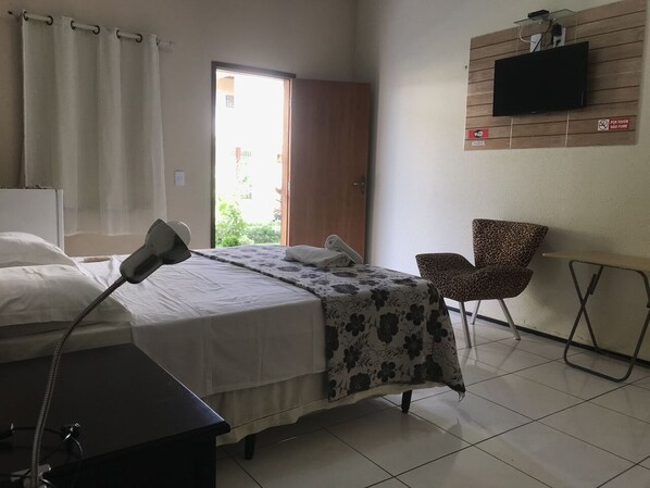 Une chambre d’hôtel avec un lit, un bureau doté d’une lampe, un téléviseur fixé au mur et un fauteuil à motifs léopard.