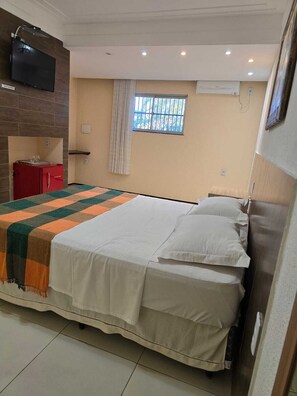 A bedroom with a bed, a TV mounted on the wall, a window with curtains, and a red cabinet. - Pousada Itarema Residence (Itarema)