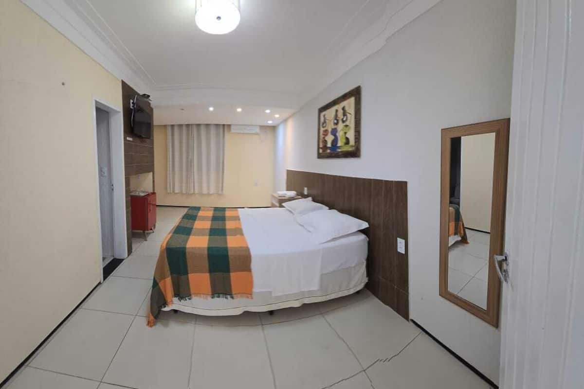 A bedroom with a bed, a checkered blanket, a wooden headboard, a mirror, and a door.