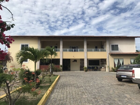 A two-story building with a paved entrance and a car parked in front. - Pousada Itarema Residence (Itarema)