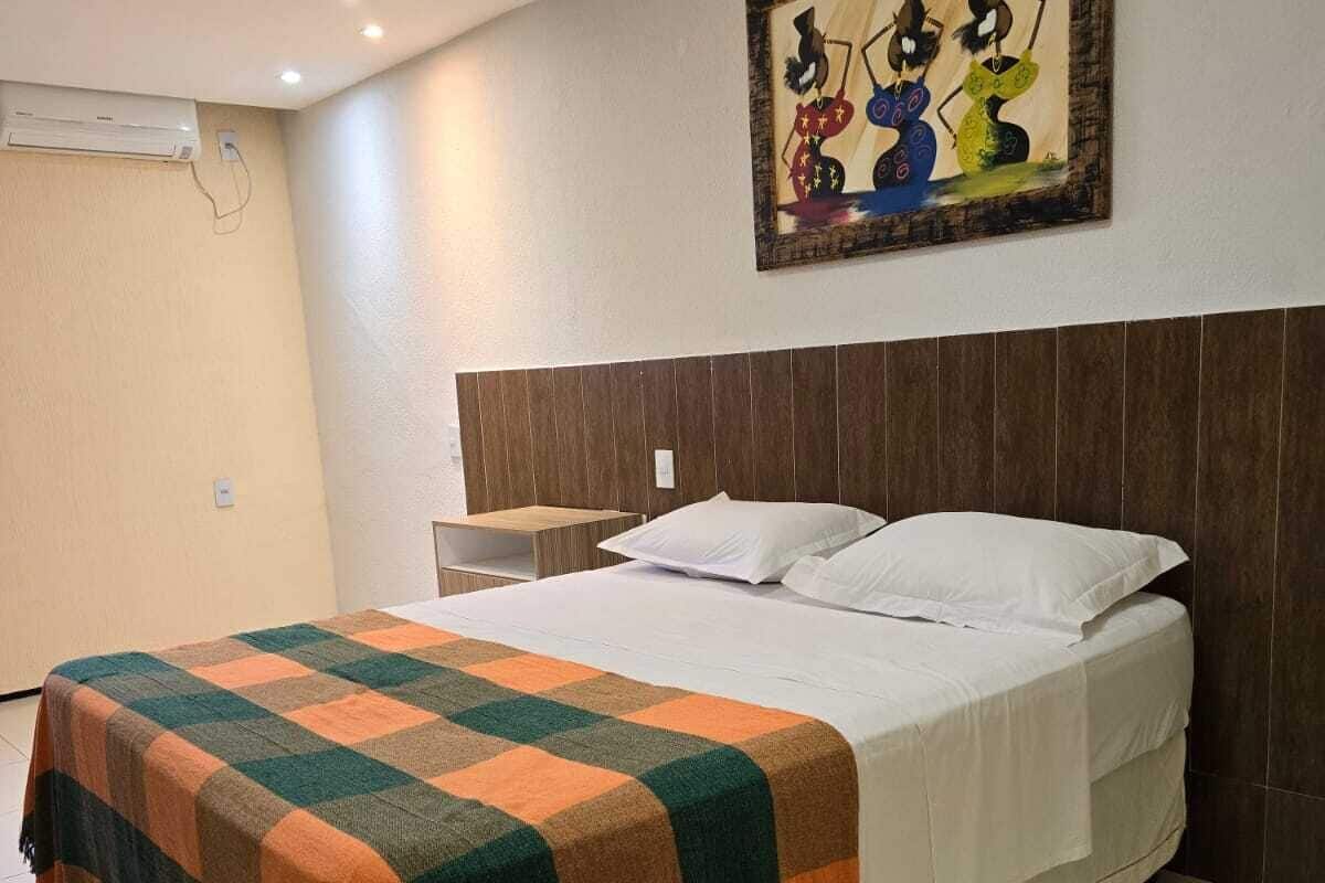 A hotel room with a large bed, a wooden headboard, a nightstand, and a painting on the wall.