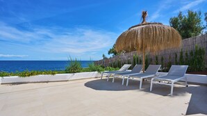 A rooftop terrace with three lounge chairs, a thatched umbrella, and a view of the sea. - Lago Spectacular Villa on the Seafront (Cala D'or)
