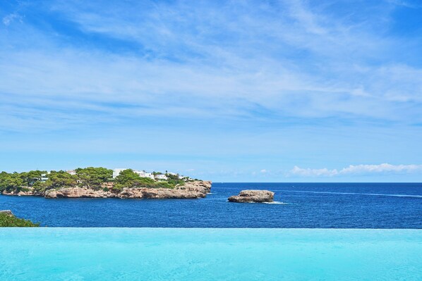 A coastal view with a clear sky, a rocky shoreline, and a swimming pool.