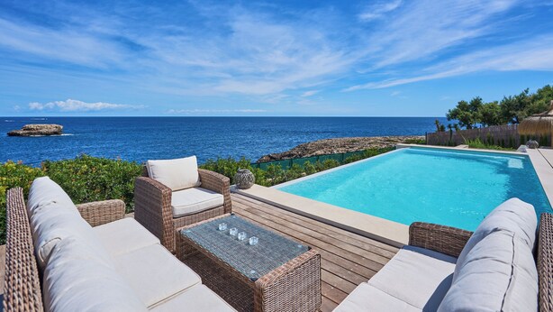 A poolside area with wicker furniture, a clear view of the ocean, and a wooden deck. - Lago Spectacular Villa on the Seafront (Cala D'or)