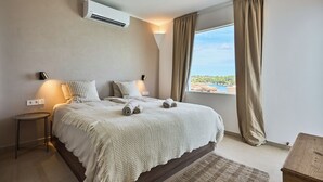 A bedroom with a bed, bedside lamps, an air conditioner, a window with curtains, and a view of the outdoors. - Lago Spectacular Villa on the Seafront (Cala D'or)