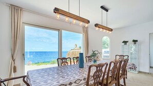 A dining area with a large table, chairs, and pendant lights. - Lago Spectacular Villa on the Seafront (Cala D'or)