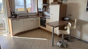A compact kitchen with a dining area, featuring a built-in oven, microwave, and a small dining table with two chairs. - Apartment in Rechlin by Muritz National Park (Rechlin)