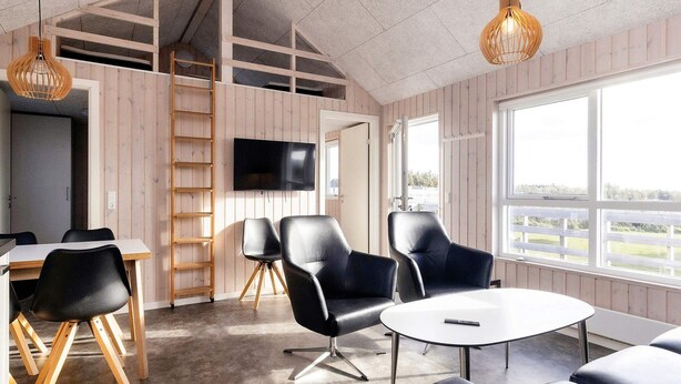 A modern interior with a wooden floor, a round table, and black leather chairs. There is a TV mounted on the wall and a ladder leaning against the wall. - Peaceful Cabin in Camping Resort (Lokken)