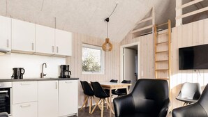 A modern kitchen with white cabinets, a coffee maker, and a dining area with black chairs and a wooden table. - Peaceful Cabin in Camping Resort (Lokken)