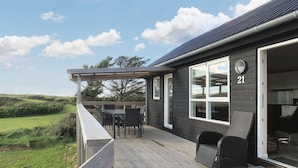 A wooden deck with outdoor furniture, a large window, and a view of the landscape. - Peaceful Cabin in Camping Resort (Lokken)