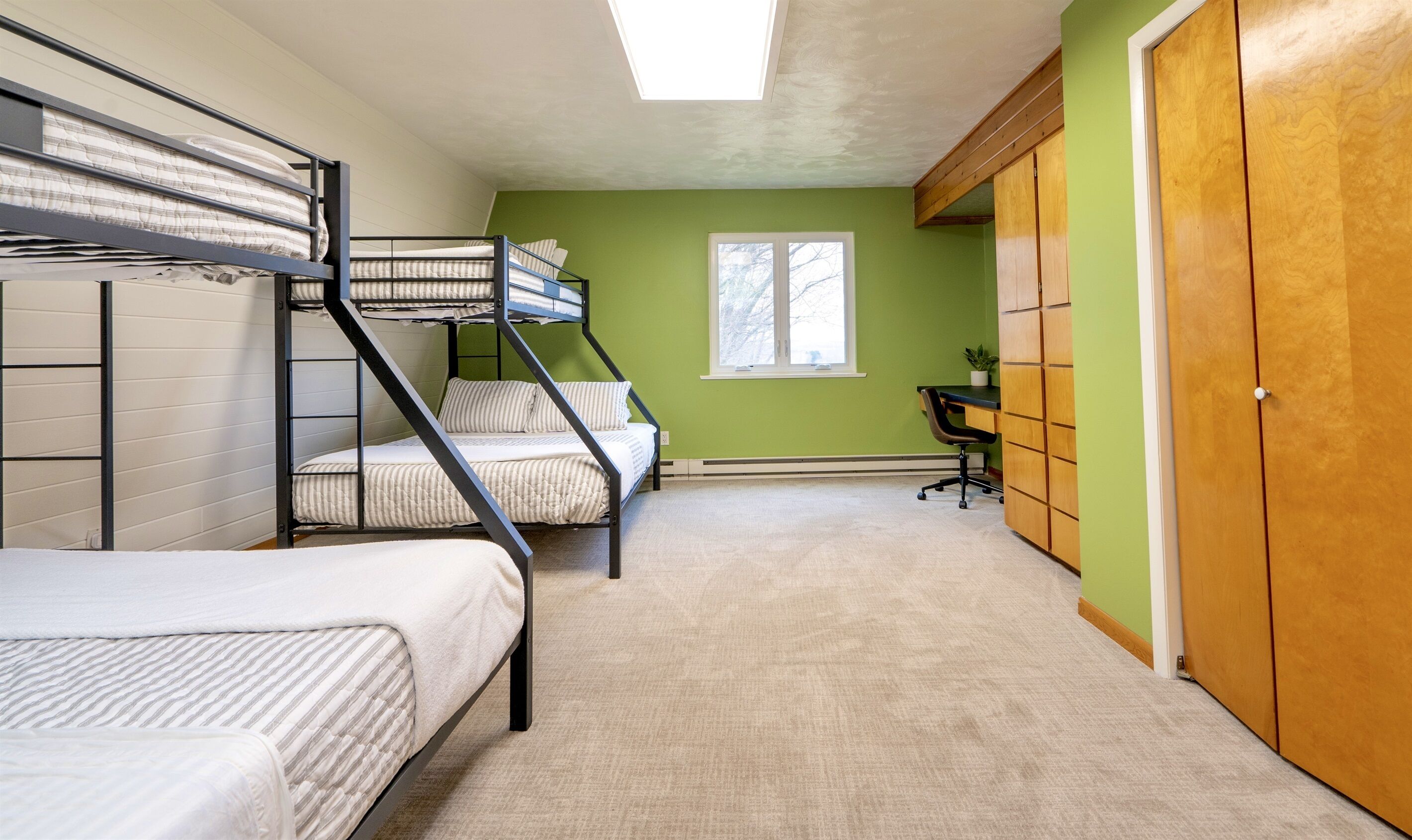 A dormitory room with bunk beds, a desk, and a window.