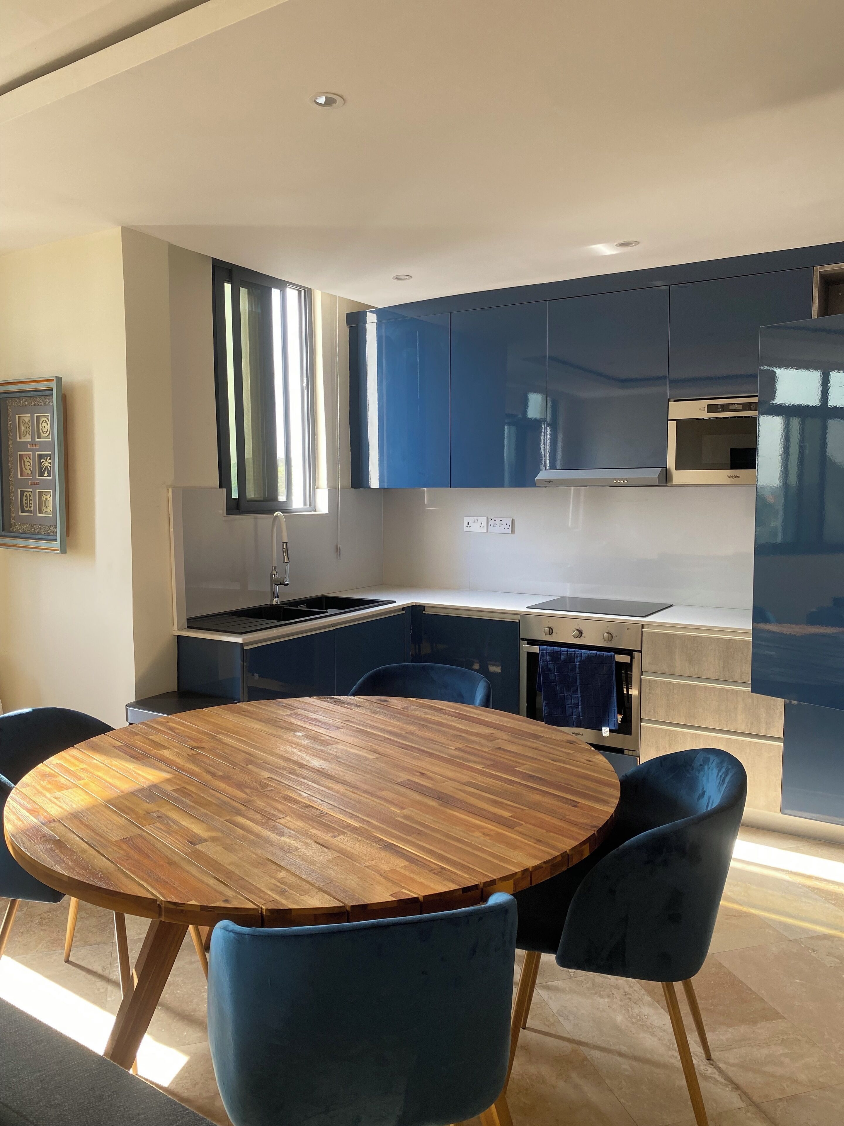 A modern kitchen with blue cabinets, a wooden dining table, and blue chairs.