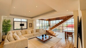 Un salon spacieux avec un grand canapé d’angle, une table basse et un escalier menant à l’étage supérieur.