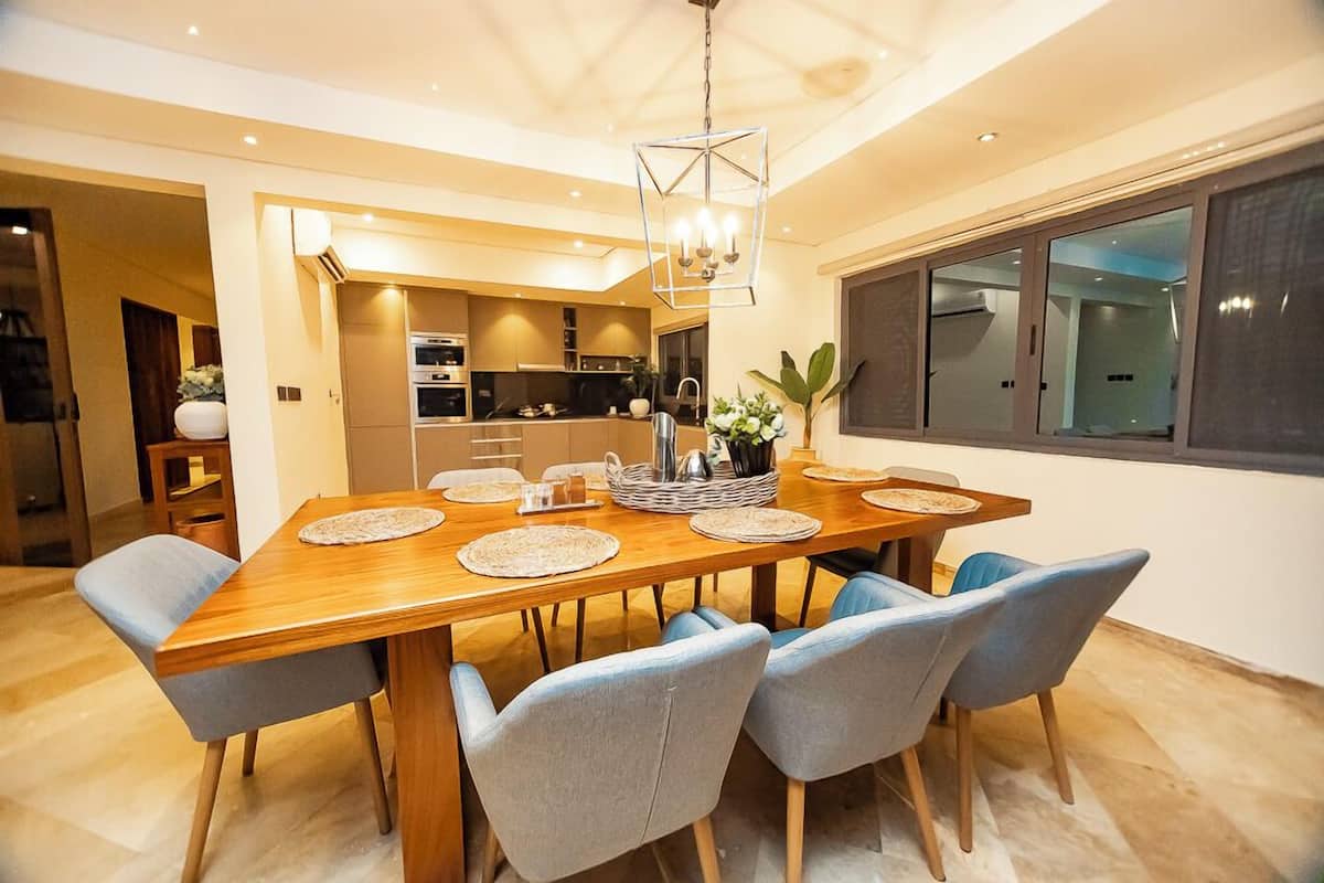Un coin repas comprenant une table en bois, six chaises et un lustre.