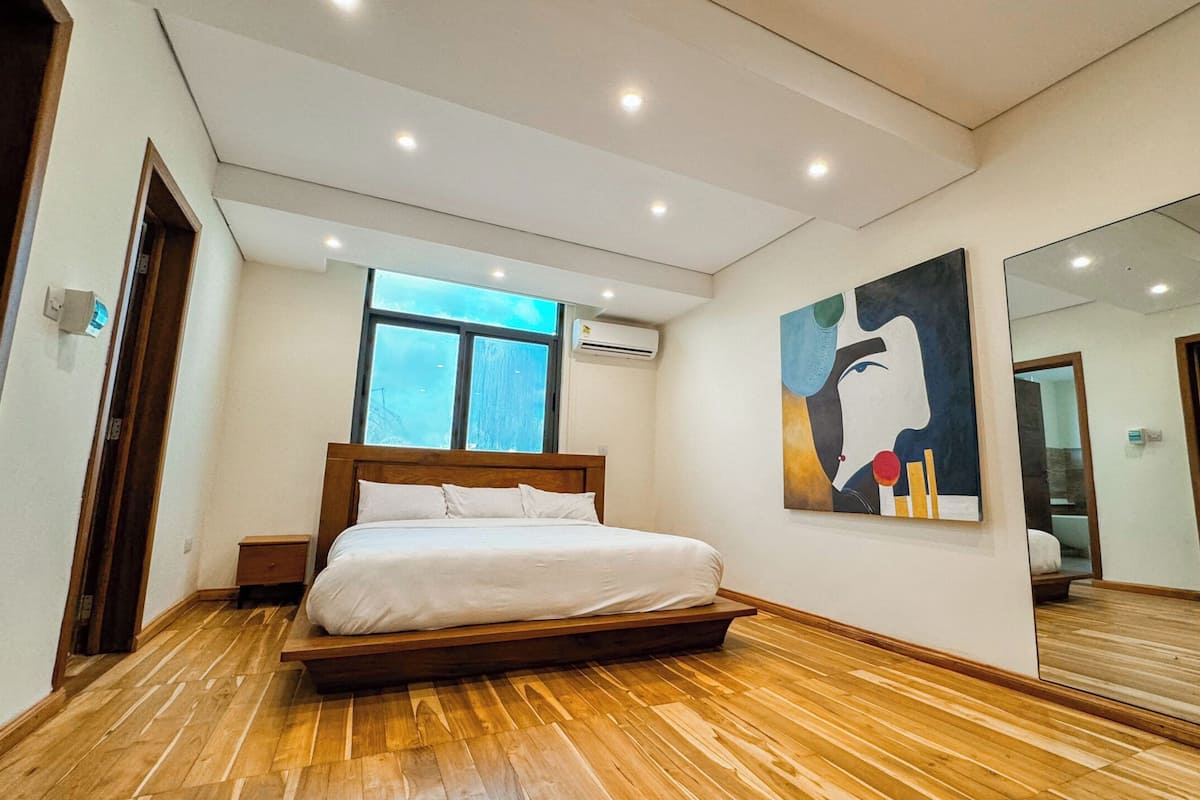 Une chambre moderne avec un plancher en bois, un grand lit, une fenêtre et un tableau au mur.