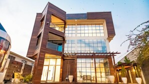 Un bâtiment moderne à plusieurs étages, doté de grandes fenêtres, d’un espace extérieur couvert et de plantes en pot.
