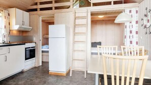 Cocina compacta con refrigerador, estufa y lavadero. Una mesa de comedor con sillas está ubicada cerca de la cocina.