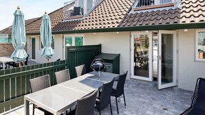 Eine Terrasse mit Tisch, Stühlen, einem Grill und Sonnenschirmen.