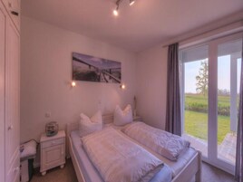 Un dormitorio con una cama doble, una mesita de noche con lámpara, un cuadro en la pared y vistas a un paisaje verde a través de una puerta corrediza.