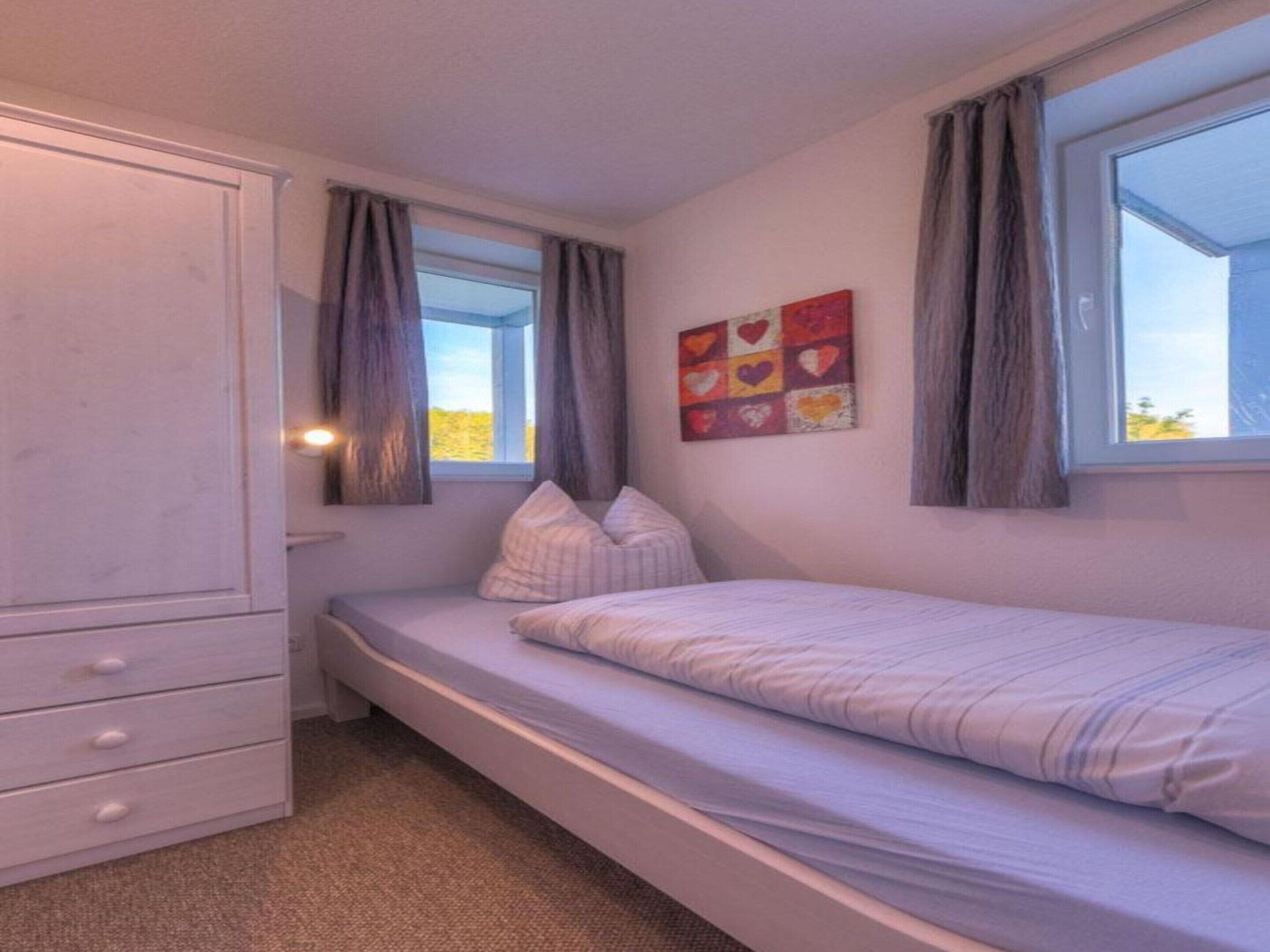 A small, single-bed room with a window, a wardrobe, and a wall art piece.