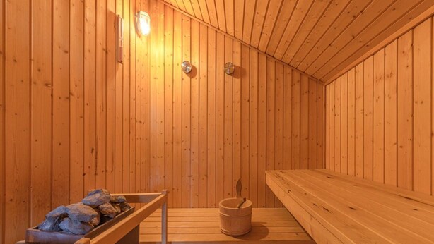Sauna, jossa on puuseinät ja -lauteet, ämpäri sekä kivillä varustettu laveri.
