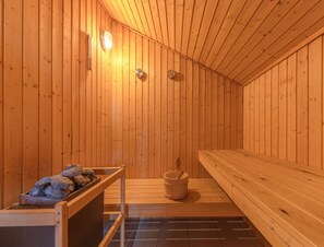 A sauna with wooden walls and benches, a bucket, and a bench with rocks. - Ferienhaus im Skandinavischen Stil (Mirow)
