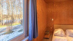 Puinen mökkimäinen huone, jossa on sänky, pieni pöytä ja ikkuna, josta avautuu näkymä lumiseen maisemaan.