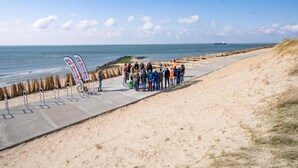 Un paseo marítimo costero con un grupo de personas reunidas, una bicicleta y una bandera.