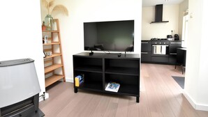 Una sala de estar moderna con un televisor de pantalla plana, estanterías de madera y una cocina con armarios negros y estufa.