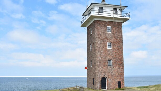Un faro de ladrillo con un balcón, una puerta y un ventanal pequeño.