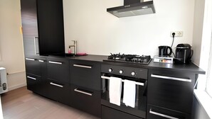 Una cocina moderna con armarios negros, horno empotrado, estufa a gas y campana extractora de acero inoxidable.