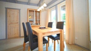 Zona pranzo con tavolo in legno e quattro sedie, una vetrina e una finestra con tende.