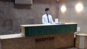 A reception desk labeled "RECEPTION" in a lobby with a marble floor and a plain wall. - Hotel Apex Inn (Vapi)