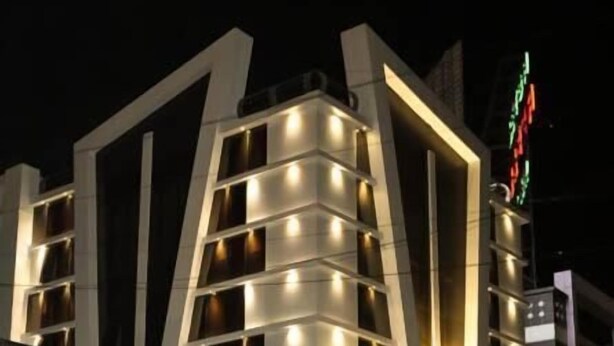 A modern hotel with a unique architectural design, featuring multiple balconies and illuminated windows. - Hotel Apex Inn (Vapi)