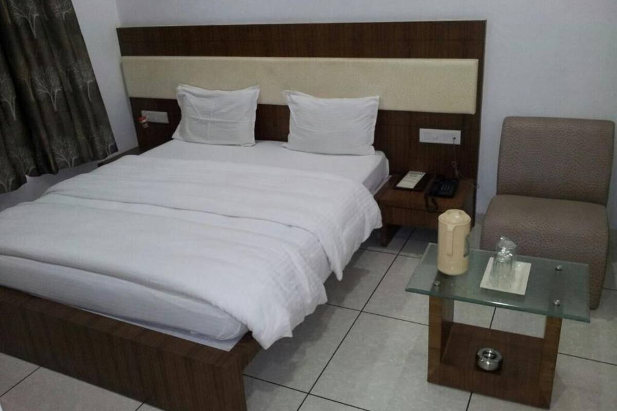 Una habitación de hotel con una cama, una silla, una mesita de noche y una mesa de vidrio con una vela.