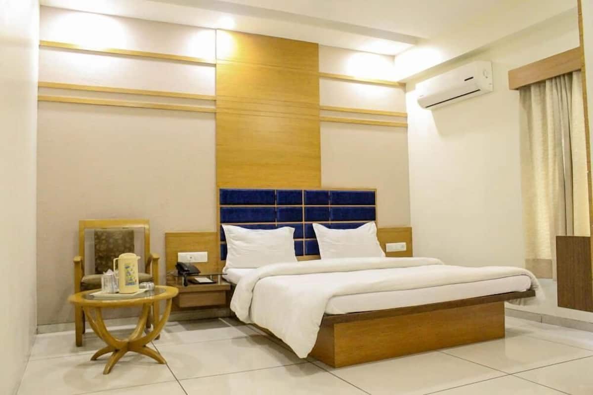 Una habitación de hotel con una cama, una mesita de noche con lámpara, una silla y una pequeña mesa con jarrón.