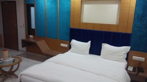 A hotel room with a large bed, a bedside table, a small round table, and a mirror. - Hotel Apex Inn (Vapi)