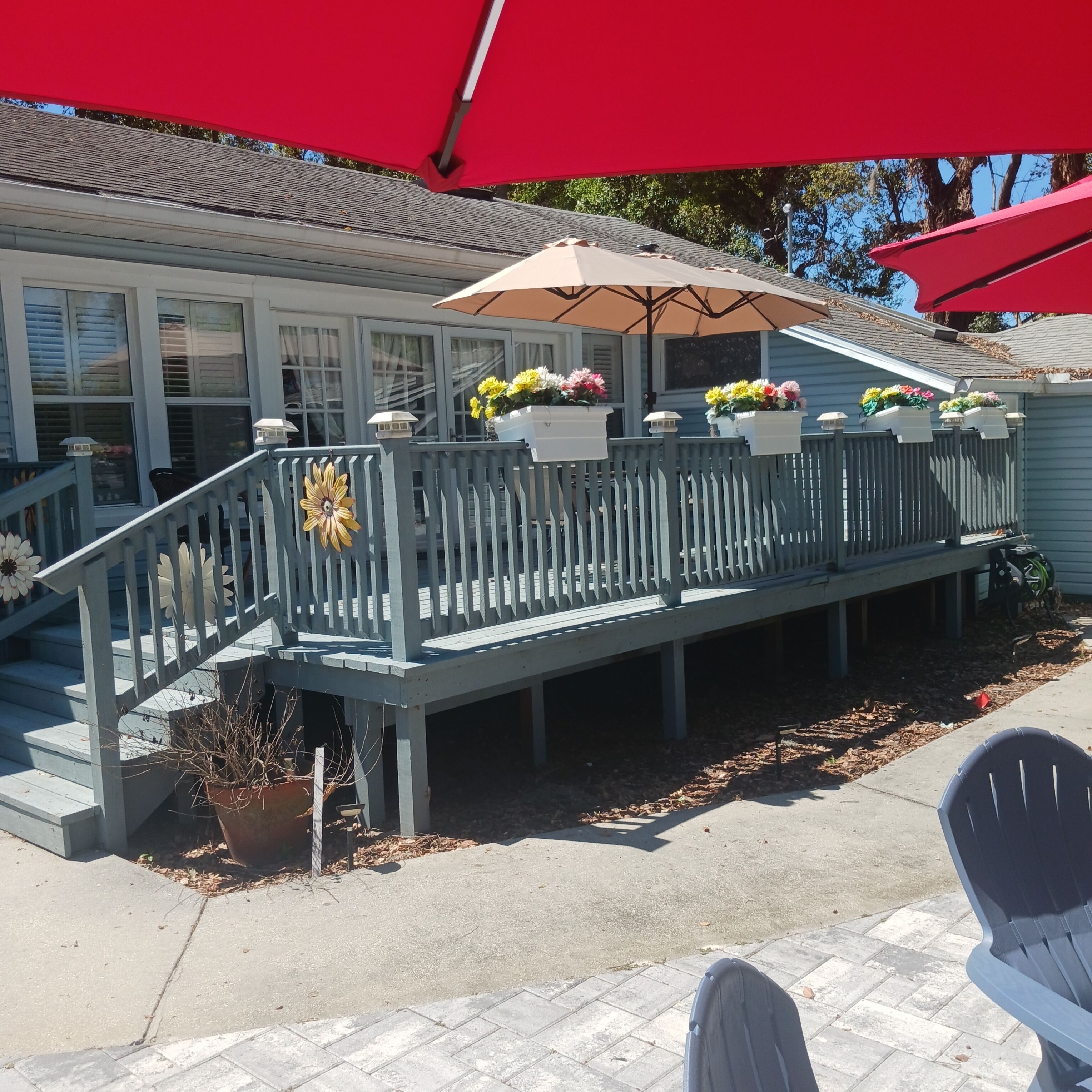 A covered deck with potted flowers, a staircase, and a red umbrella.