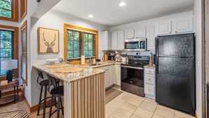 A modern kitchen with white cabinets, a black refrigerator, and a large island with bar stools. - 376 Disciples Village | Game Room | Fireplace | Walking Distance to Slopes! (Boyne Falls)