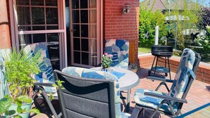 A patio area with a table and chairs, a grill, and a potted plant. - Doppelhaushalfte in Nessmersiel (Dornum)