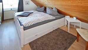A bedroom with a sloped ceiling, a bed with polka dot bedding, a small bedside table, and a window with curtains. - Doppelhaushalfte in Nessmersiel (Dornum)
