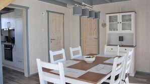 A dining area with a wooden table and white chairs, a kitchen in the background, and a cabinet with glass doors. - Skandinavisches Ferienhaus in Mirow (Mirow)