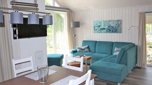 A modern living room with a teal sofa, a dining table with chairs, a flat-screen TV, and a painting on the wall. - Skandinavisches Ferienhaus in Mirow (Mirow)