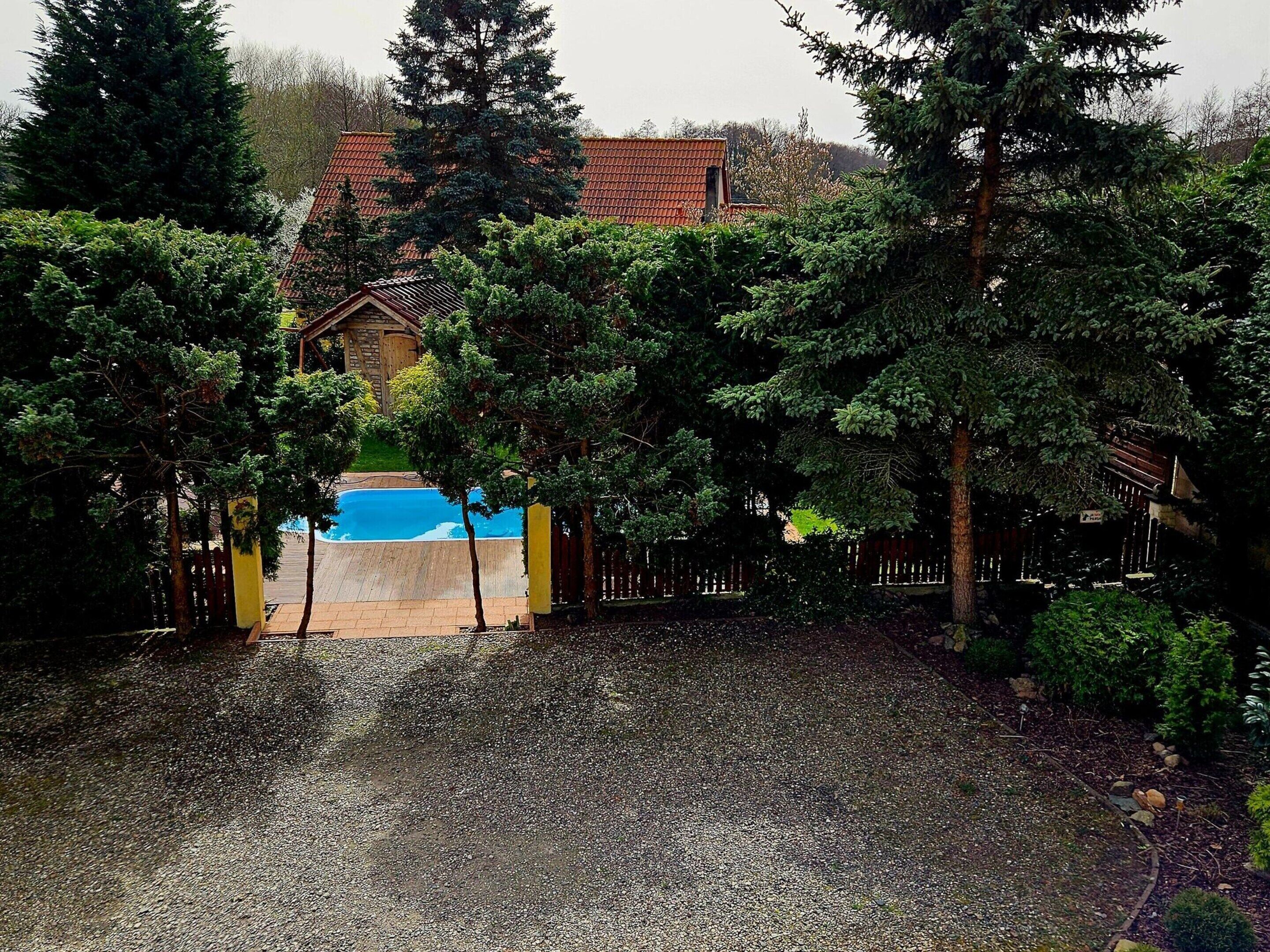 Um quintal com piscina, cercado por árvores e um muro de madeira.