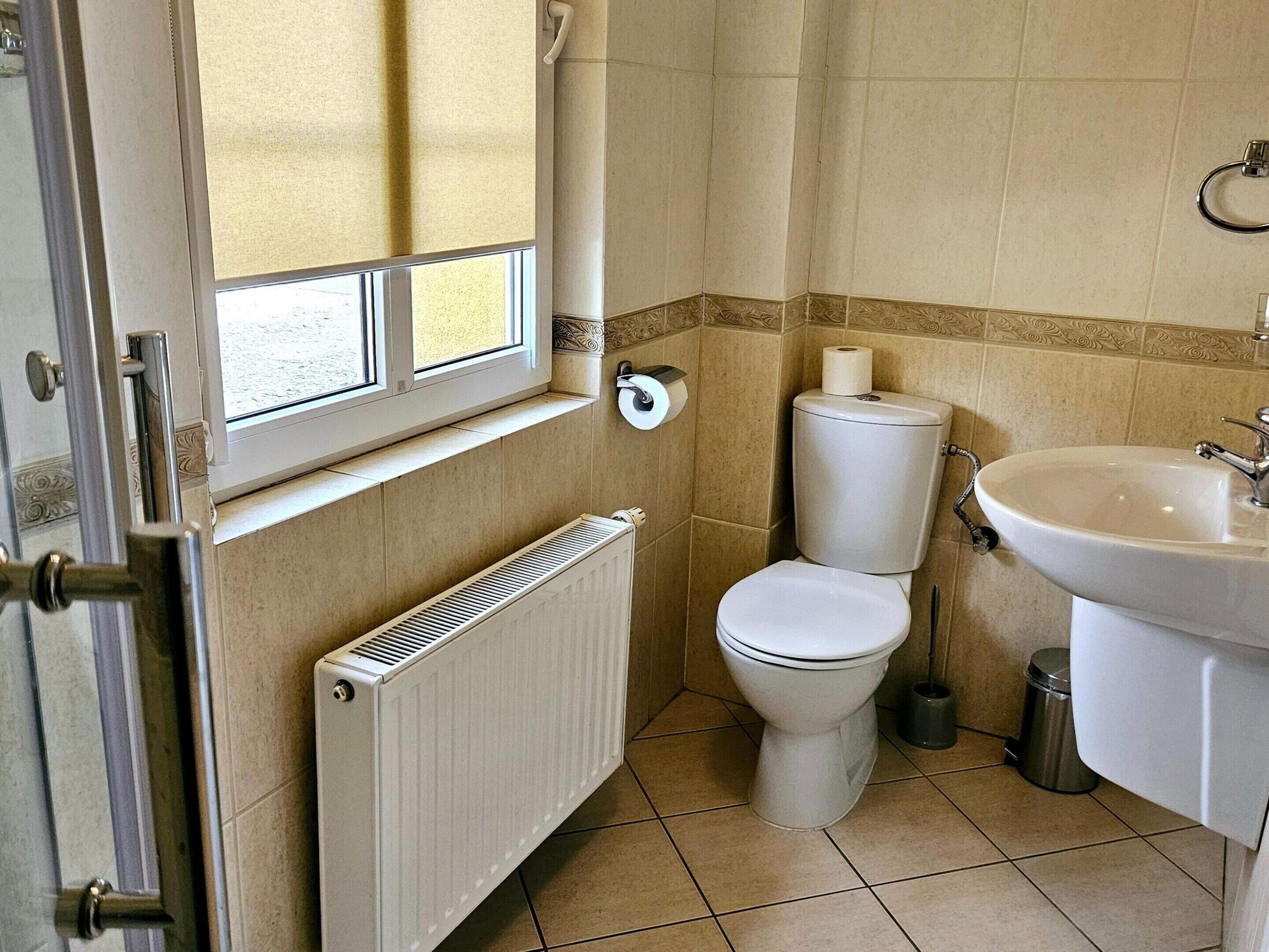 A bathroom with a toilet, radiator, sink, and a window.