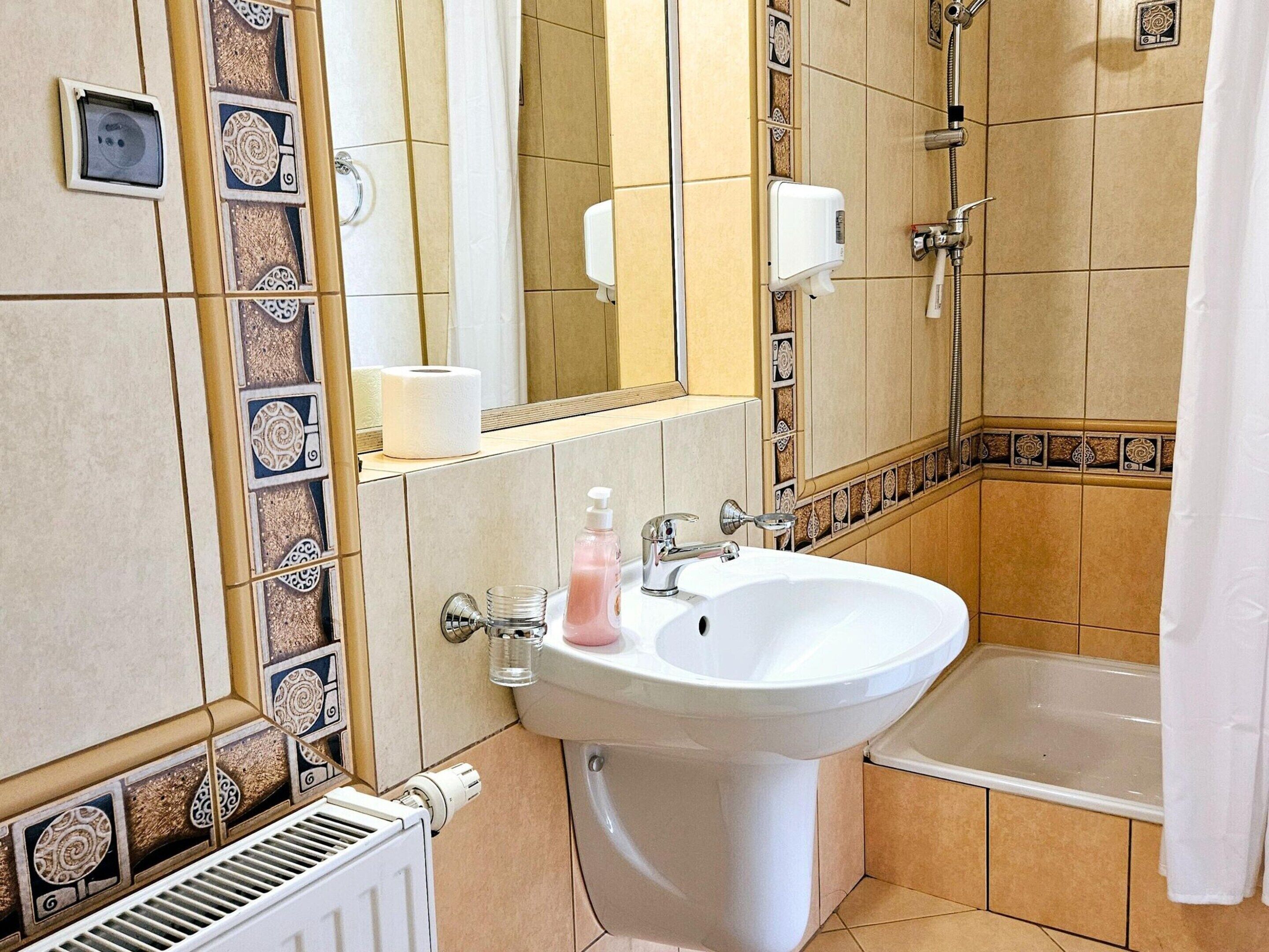 A bathroom with a white sink, a bathtub, and a toilet. There is a towel hanging on the wall and a bottle of soap on the sink.
