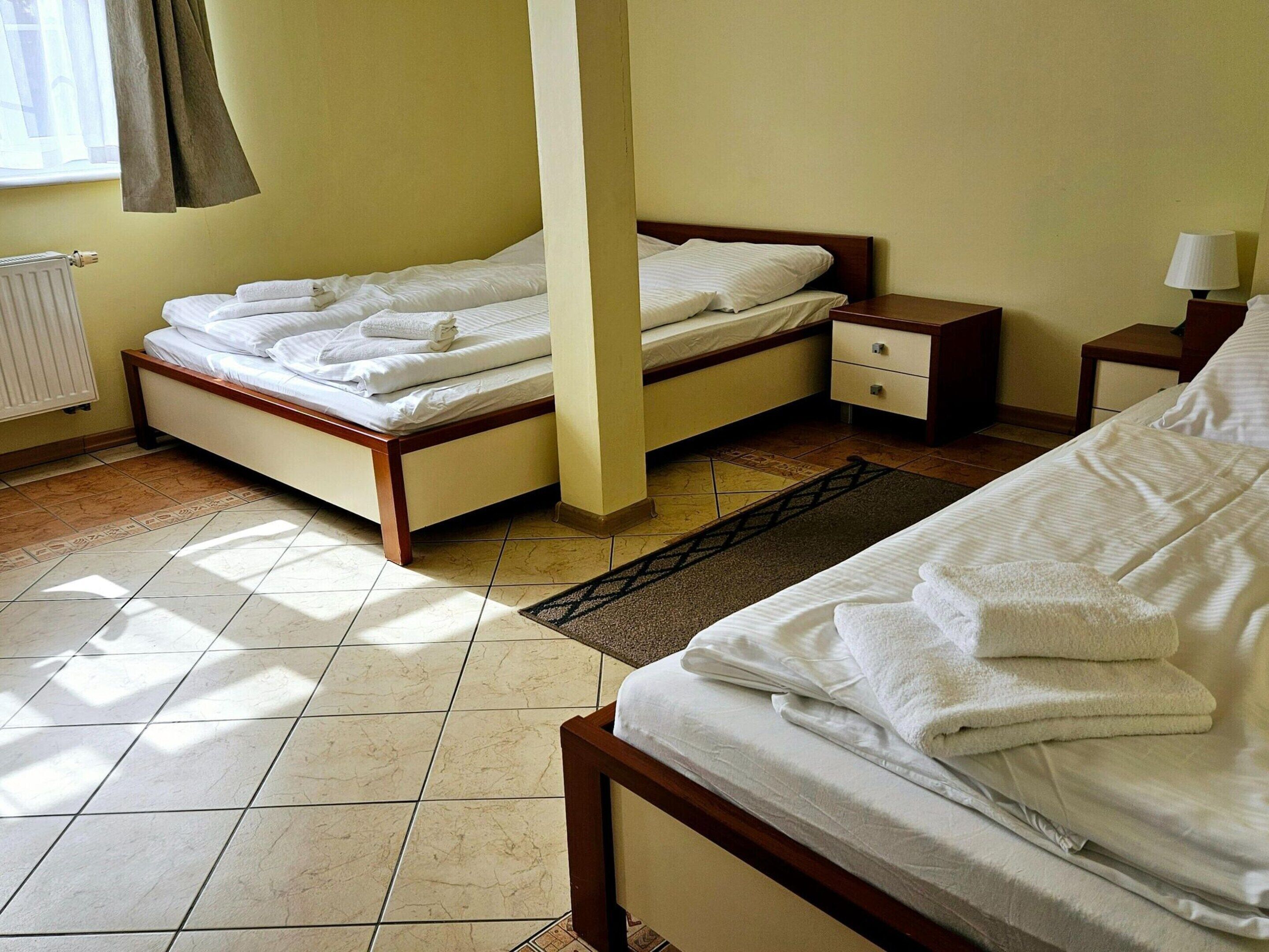 Une chambre d’hôtel avec deux lits, une tête de lit en bois, une table de chevet, une lampe et un radiateur.