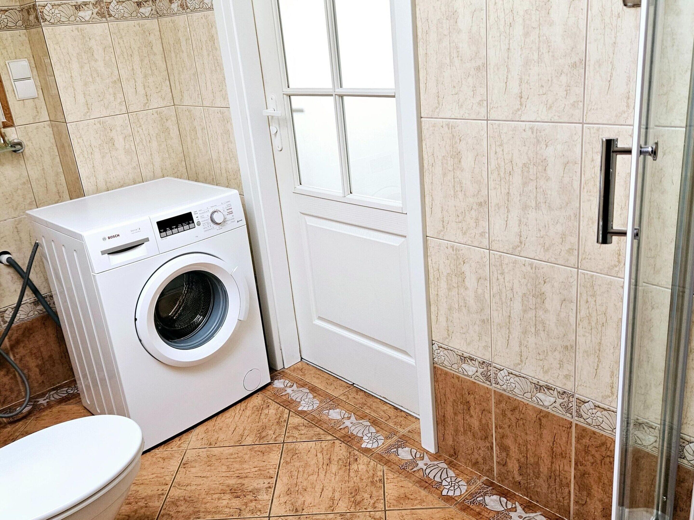 A compact bathroom with a Bosch washing machine, a toilet, and a shower area.